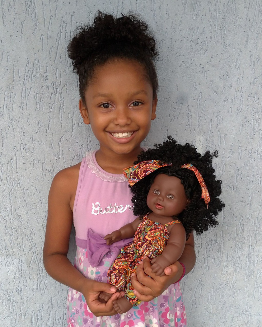 Menina negra sorrindo enquanto segura uma boneca negra e cabelos afro